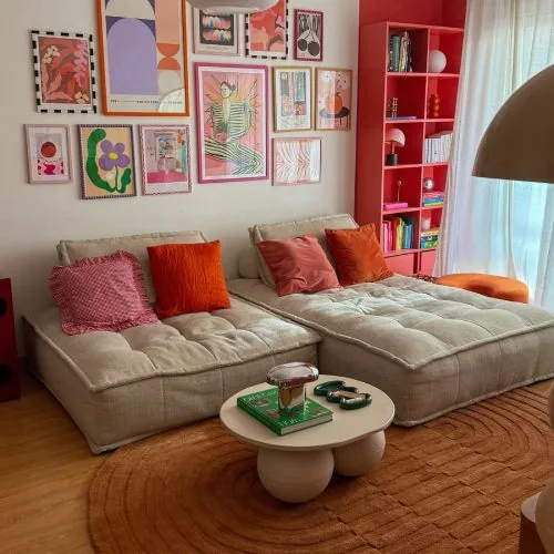 Sala de estar que combinou um grande sofá direto no chão com almofadas bem coloridas e vários quadros. Inspirações de decoração maximalista para apartamentos