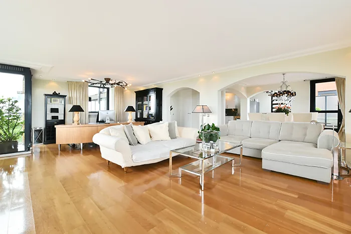 Sala de estar com piso de madeira, sofás claros e mesa de centro transparente