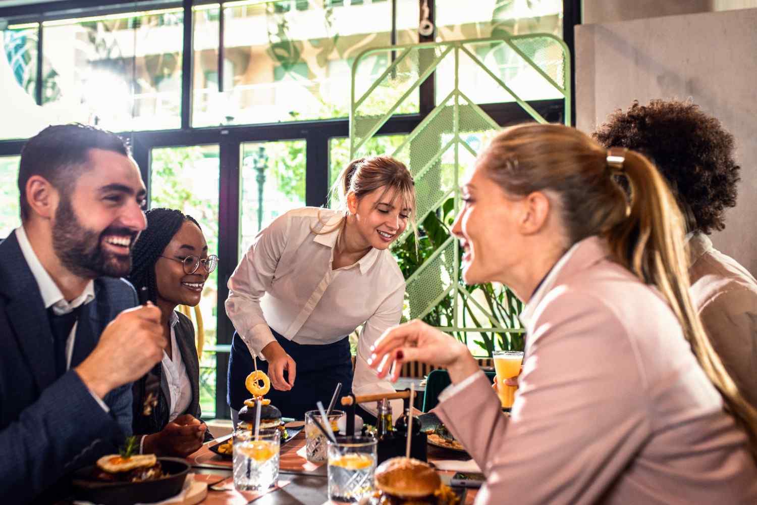 Grupo de pessoas conversando e sorrindo em um restaurante iluminado e acolhedor.