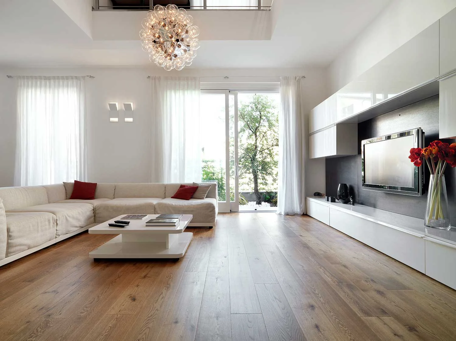 Sala de estar clara com piso de madeira, sofá branco e iluminação natural