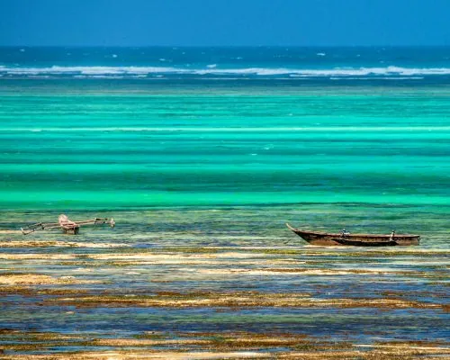 Barcos de madeira sobre águas rasas e coloridas nas praias de Zanzibar, na Tanzânia.