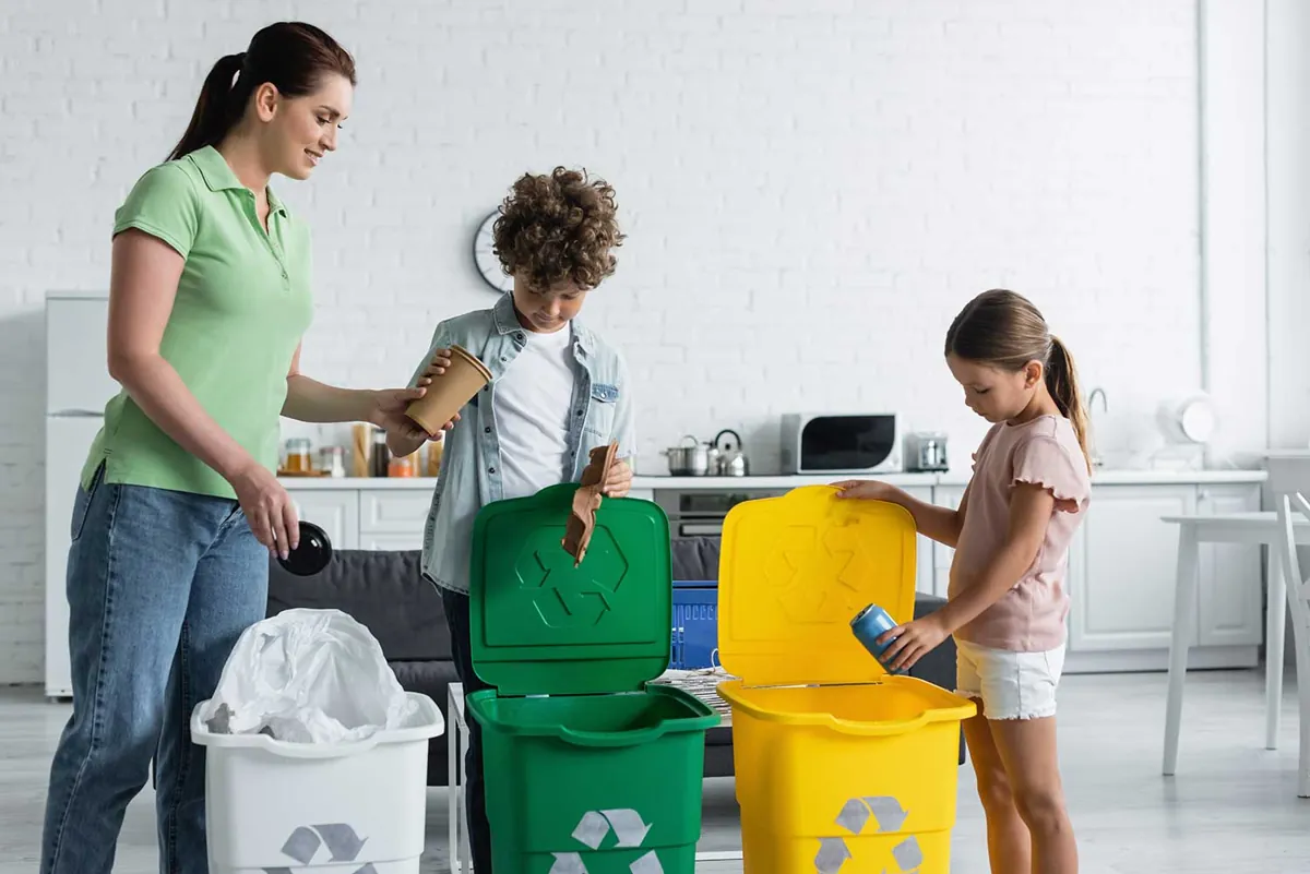 Família separando materiais recicláveis em lixeiras na cozinha de um apartamento