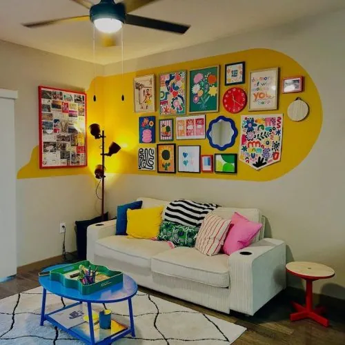 Parede atrás do sofá, com quadros e espelhos emoldurados por uma parede amarela. Inspirações de decoração maximalista para apartamentos