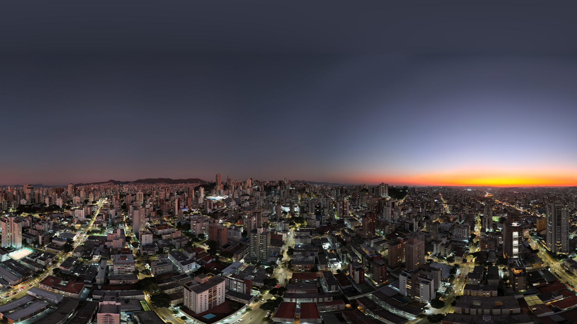 Vista panorâmica de Belo Horizonte ao entardecer, com o céu em tons de azul e laranja e a cidade iluminada, destacando a harmonia entre urbanismo e paisagem no bairro Gutierrez.