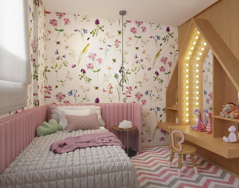 Quarto infantil com papel de parede floral, cama rosa e cantinho de brincadeiras com iluminação em formato de casinha.