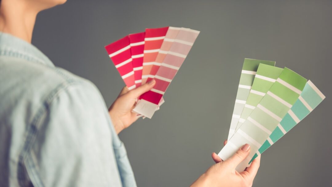 Pessoa segurando amostras de cores em tons de verde e rosa para escolher a tinta ideal para o quarto.