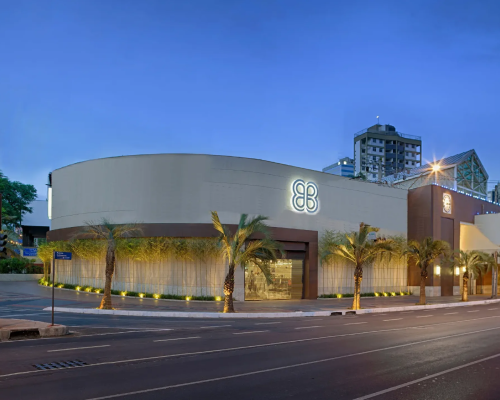 Fachada externa do Shopping Pátio Savassi ao entardecer, com iluminação suave e palmeiras ao redor.