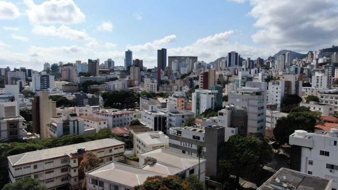 Vista aérea do bairro Anchieta em Belo Horizonte, com edifícios residenciais em meio a áreas verdes e horizonte urbano ao fundo.
