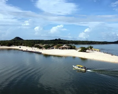 Vista aérea de praia de rio em Alter do Chão, com águas calmas, faixa de areia e barco navegando.