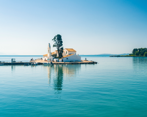 Pequena ilha com igreja branca em Corfu, Grécia, cercada por mar calmo e azul.