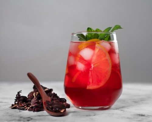 Copo com chá de hibisco, rodelas de laranja e gelo, decorado com hortelã.