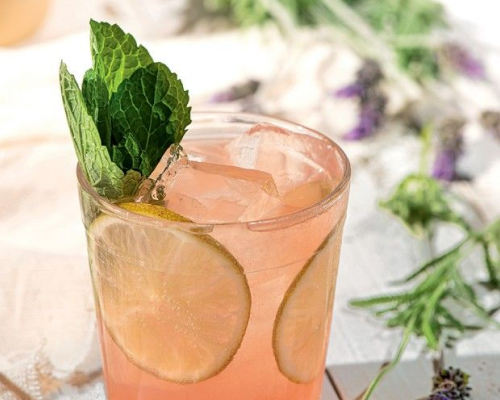 Drink com rodelas de limão, hortelã e lavanda em um copo com gelo.
